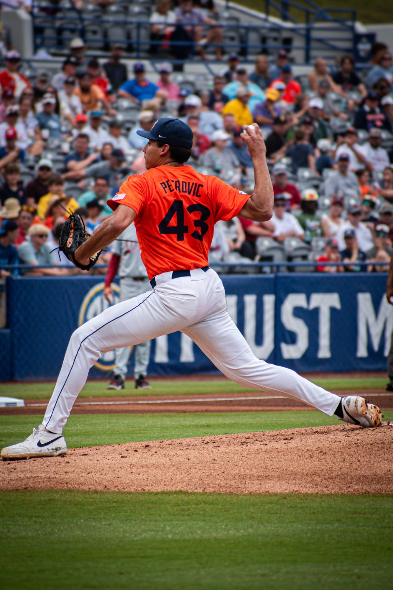 Pitcher in an orange number 43 jersey mid-delivery in front of a full stand