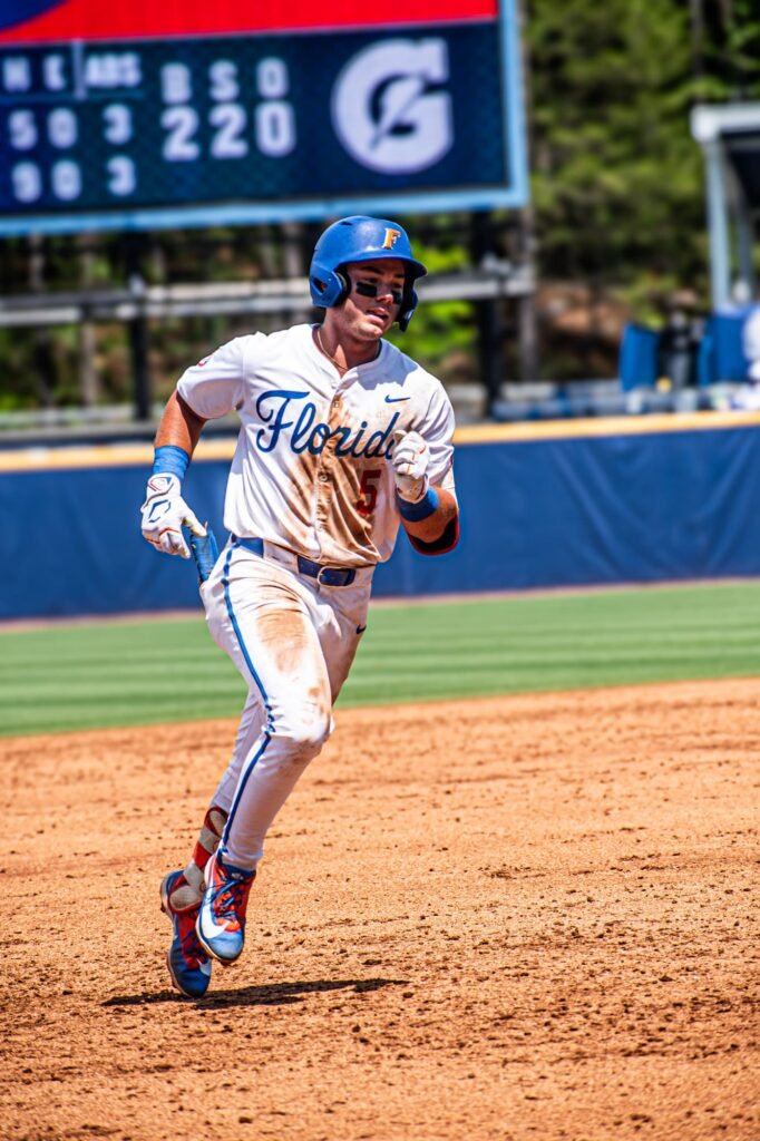 Base runner in a white and blue uniform rounding the bases
