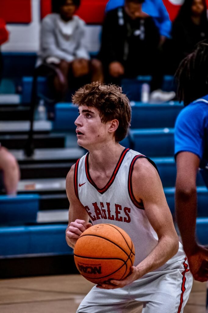 Player in a white and red jersey holding the ball, looking up court
