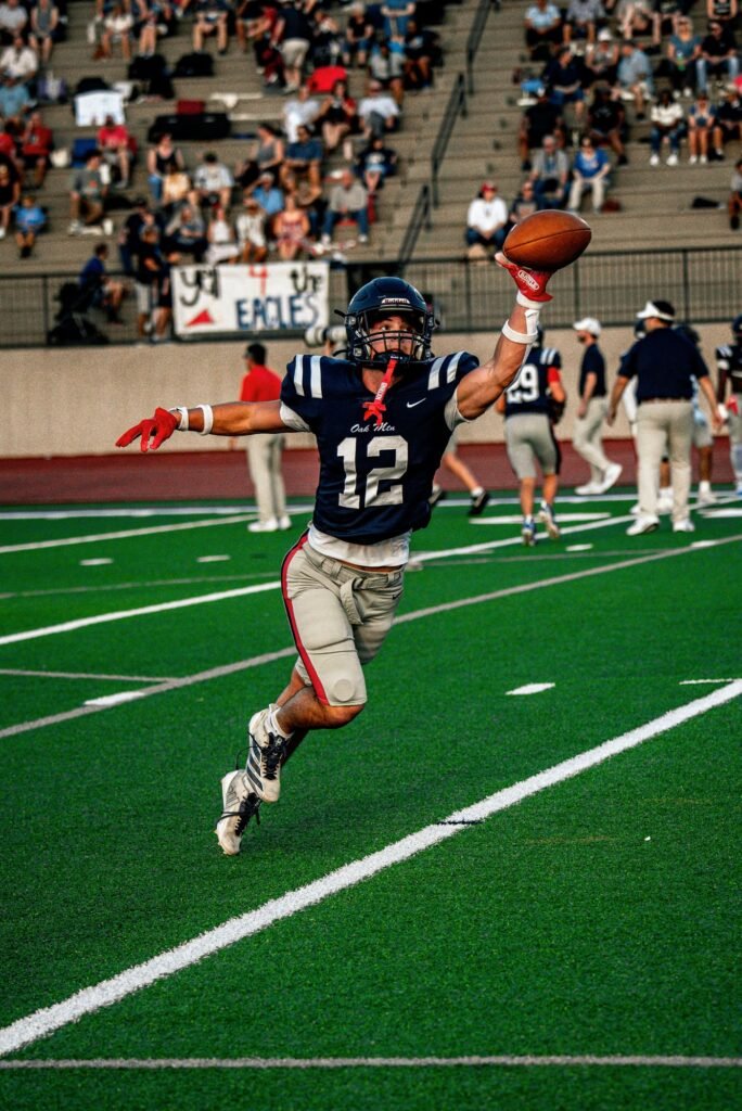 Receiver in a navy number 12 jersey catching a pass on the turf