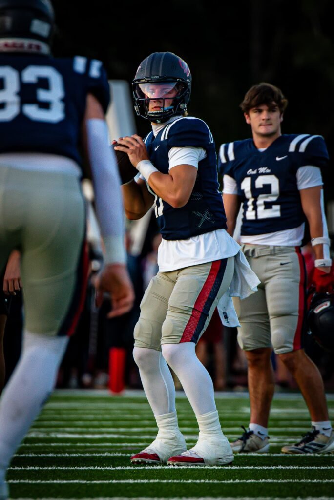 Quarterback in navy number 12 setting up to throw, a teammate in the foreground