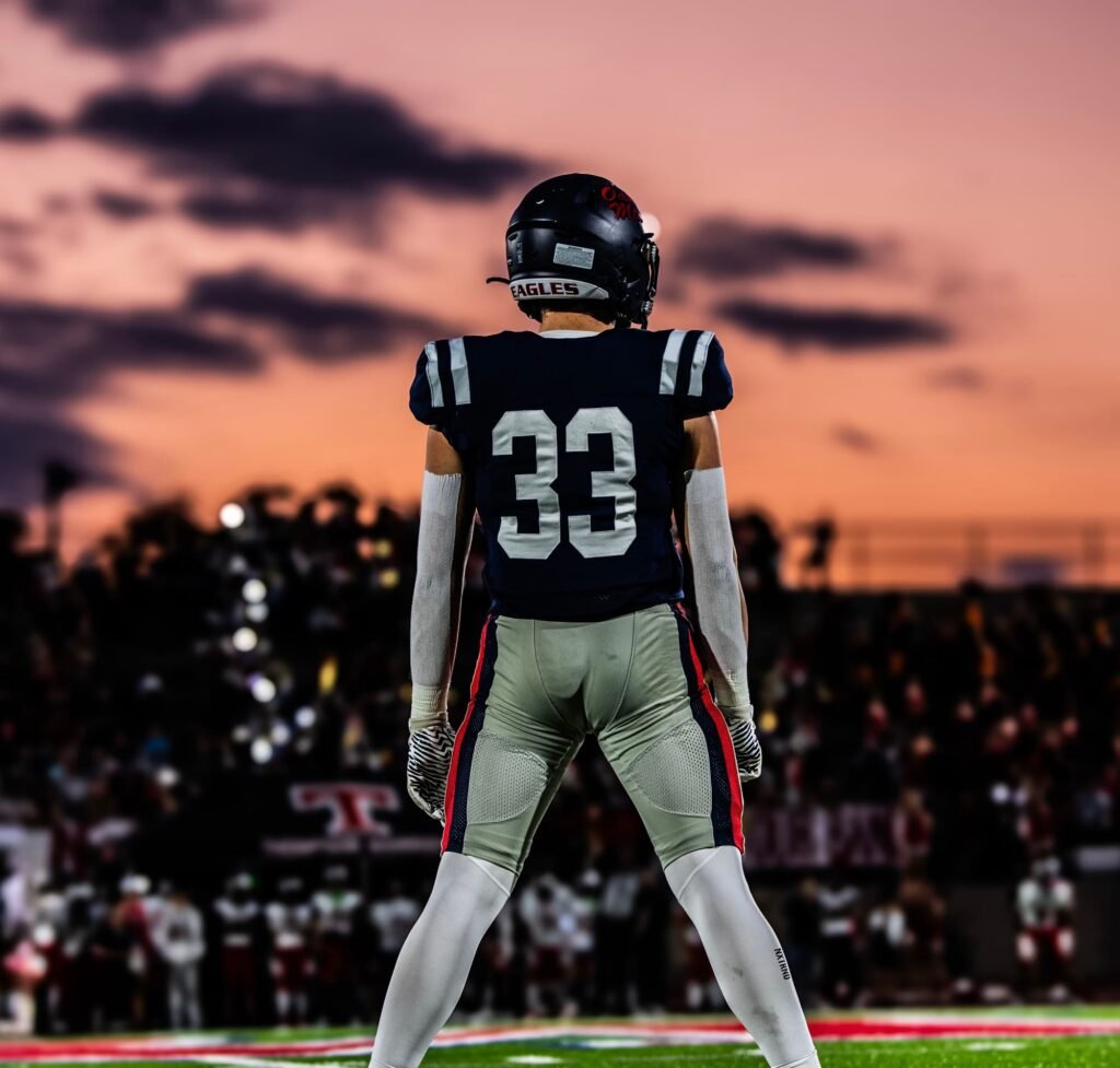 Player in a number 33 jersey from behind, facing the field under a pink evening sky
