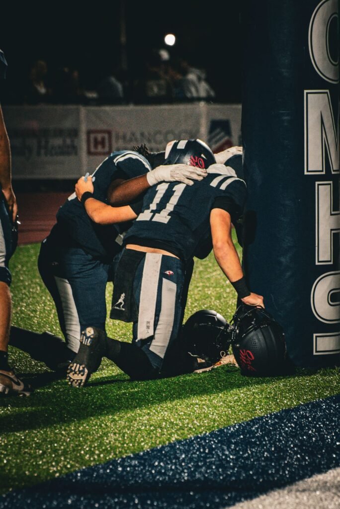 Two players kneeling on the field after the game, helmets off