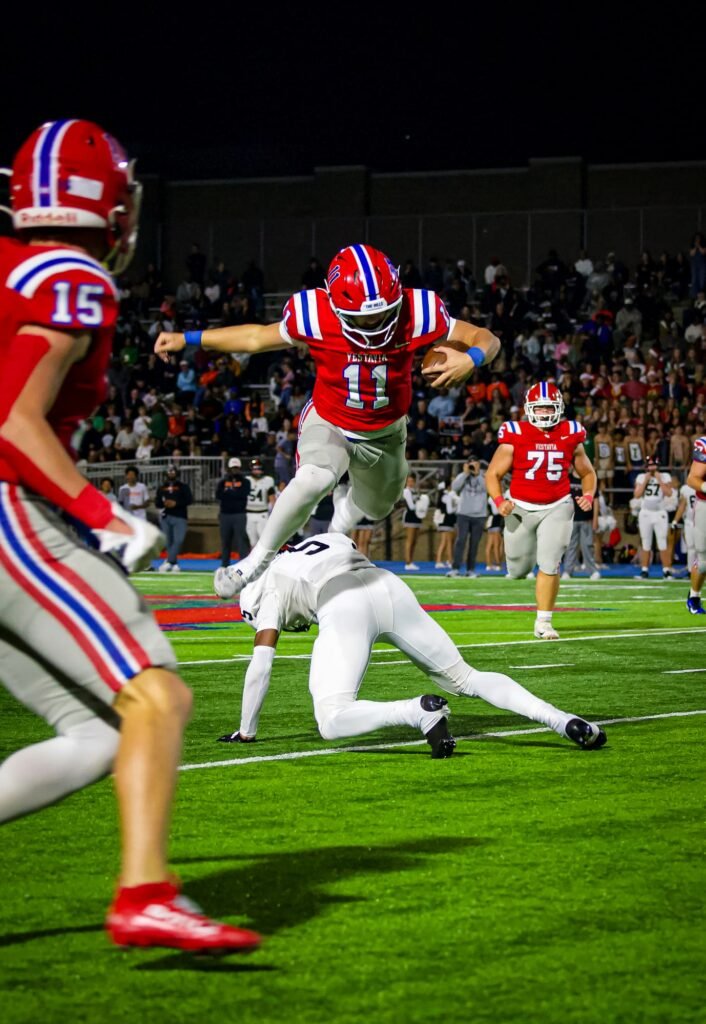 Player in a red number 11 jersey hurdling a defender at the line