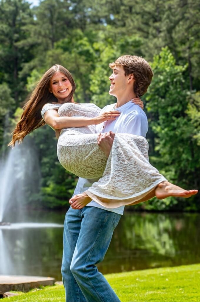 He lifts her off the grass, both laughing, a fountain behind them