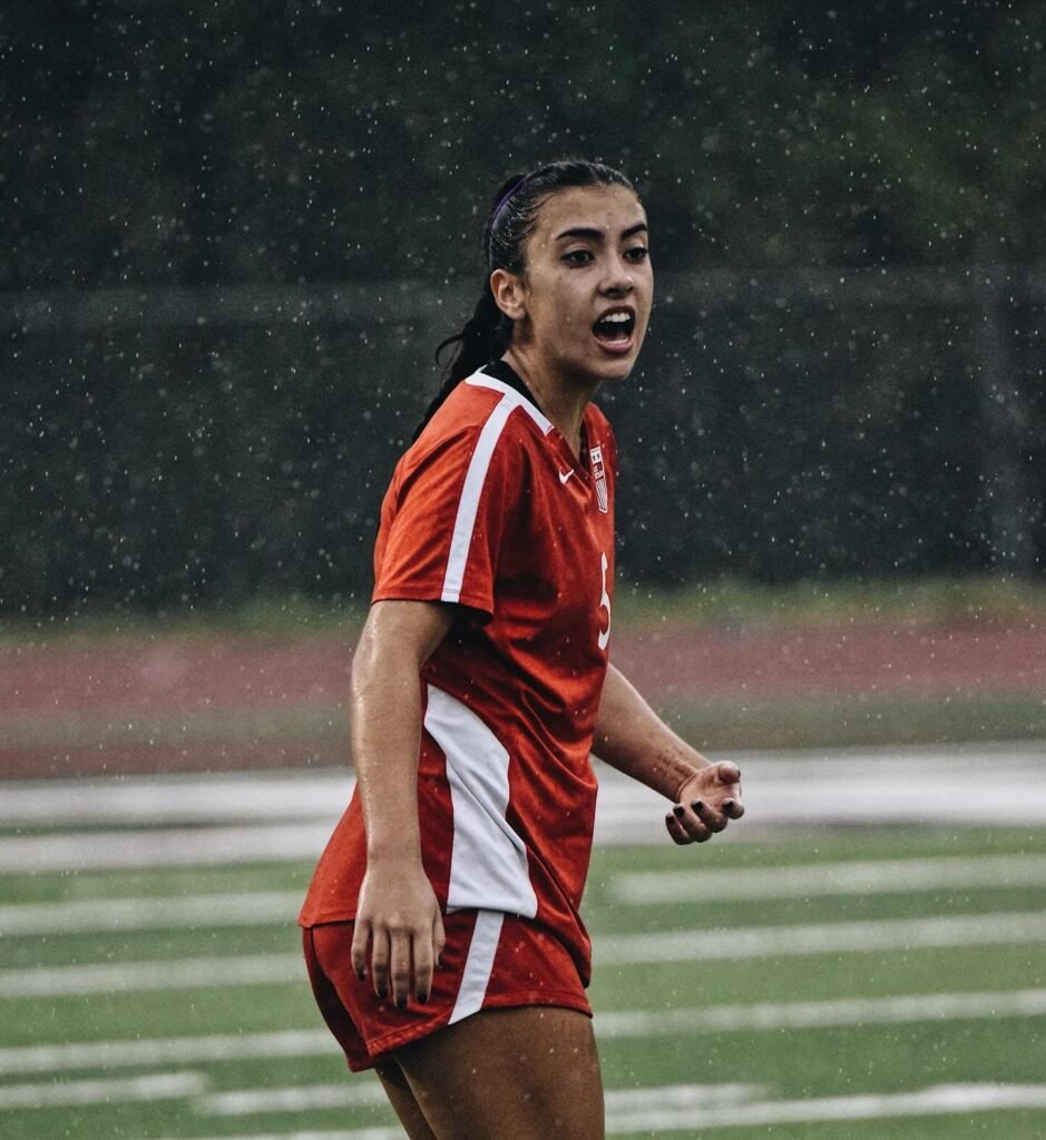 Soccer player in a red kit shouting in the rain
