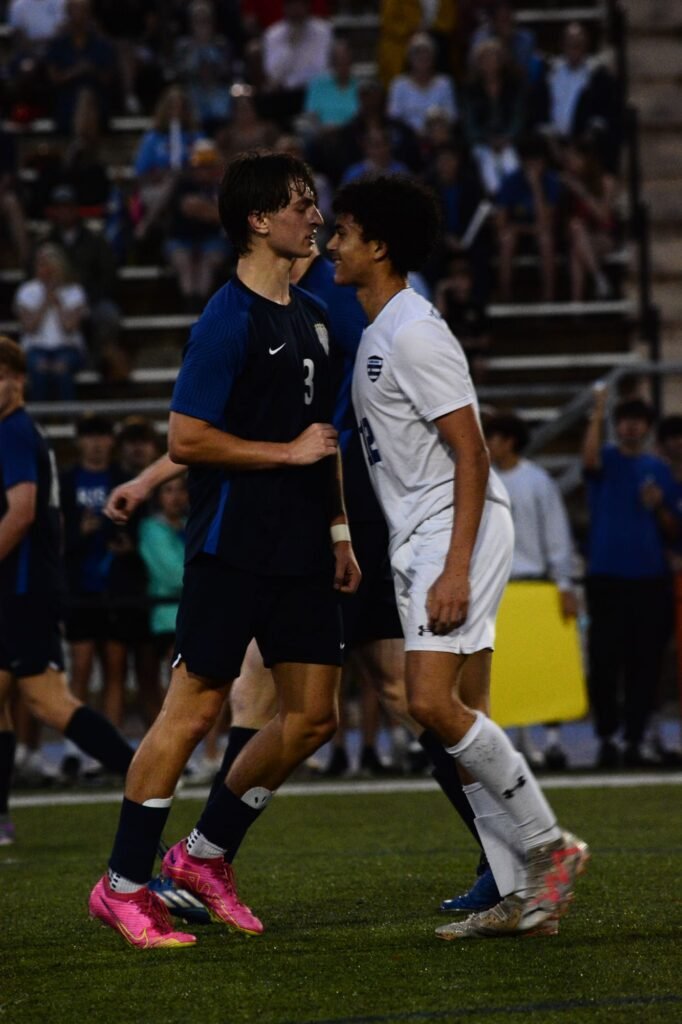 Two soccer players in navy and white talking on the field