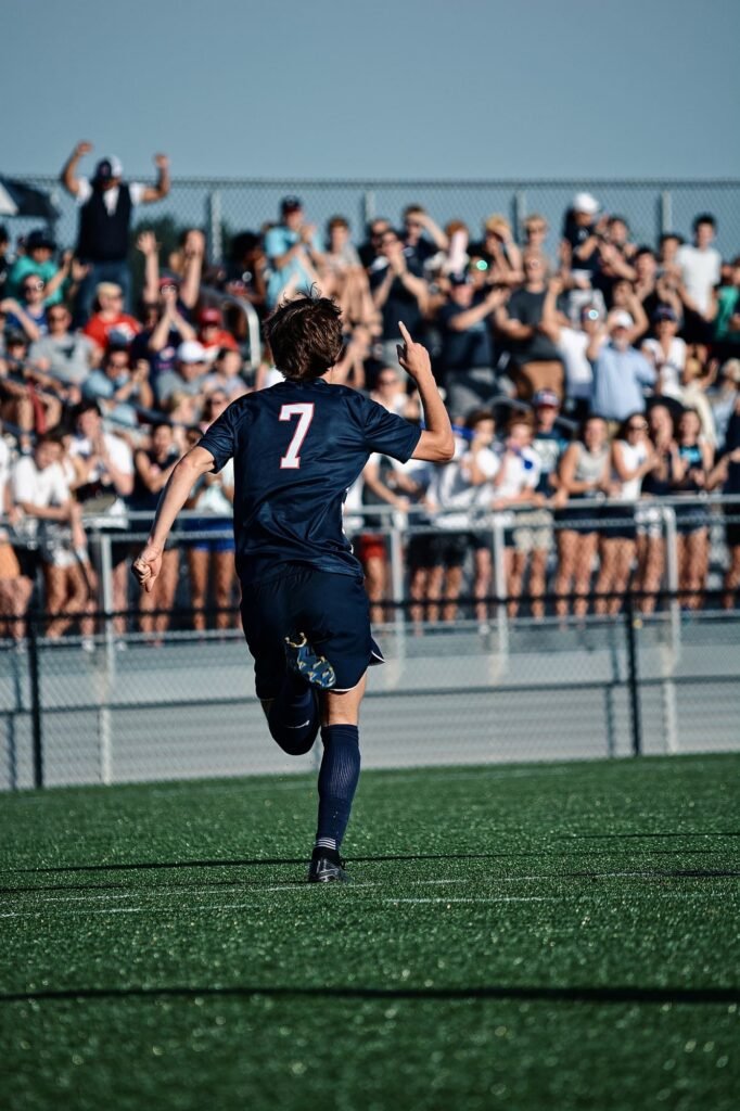 Player in a navy number 7 shirt running past the stand, pointing to the crowd