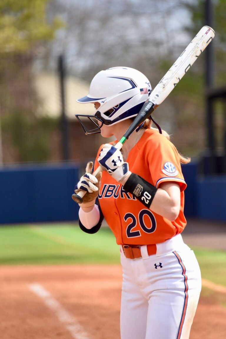 Softball batter in an orange number 20 jersey and helmet waiting on a pitch